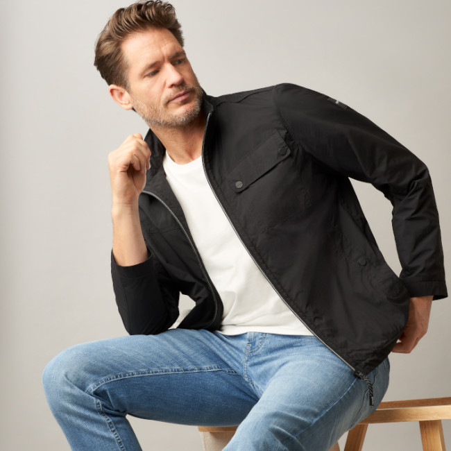 Ein Mann eine dunkle Jacke und sitzt auf einem Stuhl